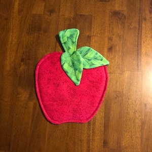 May include: A red apple-shaped pot holder with a green leaf design. The pot holder is made of fabric and has a quilted texture.