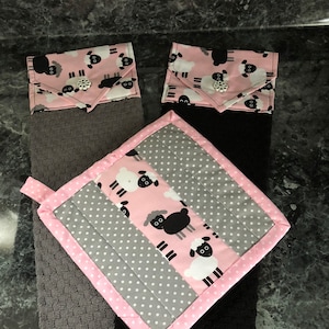 May include: Set of three kitchen towels featuring a black and white sheep design. The towels are grey, black and pink with white polka dots. The towels are trimmed with pink fabric.