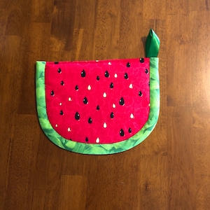 May include: A red and green watermelon-shaped pot holder with black seeds.