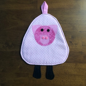 May include: Pink and white polka dot pot holder with a pink pig face and black button eyes. The pot holder has a loop for hanging and two black fabric legs.