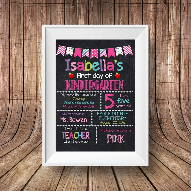 May include: A chalkboard sign with the text "Isabella's first day of KINDERGARTEN". The sign also includes information about Isabella's favorite things, her age, her teacher, and her school. The sign is decorated with colorful banners and hearts.