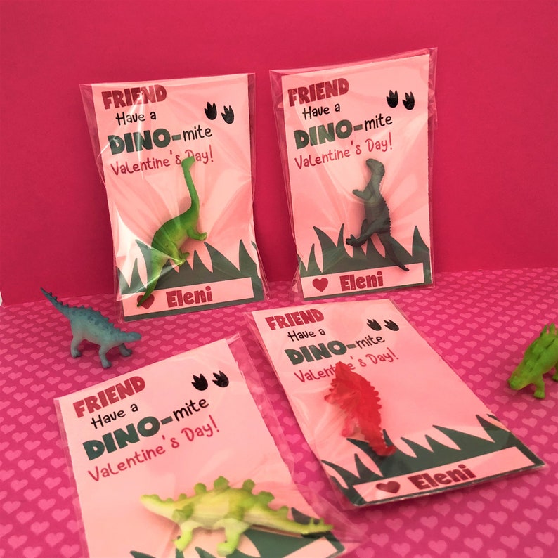 May include: Four pink Valentine's Day cards with dinosaur toys inside. Each card says "Friend Have a Dino-mite Valentine's Day!" and has a heart with the name "Eleni" on it.