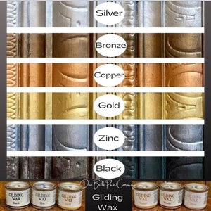 Puede incluir: Un conjunto de ocho pequeños botes de pintura metálica etiquetados con diferentes colores metálicos: plata, bronce, cobre, oro, zinc, negro. Los botes están dispuestos en fila con una muestra de cada color pintada en un marco de madera detrás de ellos. El texto "Gilding Wax" está impreso debajo de los botes.