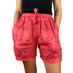 Può includere: Pantaloncini color corallo con vita con coulisse e tasche. I pantaloncini presentano un motivo ripetuto di simboli e disegni decorativi neri. I pantaloncini sono realizzati in un tessuto leggero.