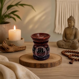 Könnte beinhalten: Ein dunkel rötlich-brauner Öl-Brenner aus Holz mit einem geschnitzten Hamsa-Hand-Symbol auf der Vorderseite. Der Brenner verfügt über einen breiten, kreisförmigen Sockel und eine schalenförmige Oberseite für Öl oder Wachs mit glatter Oberfläche.