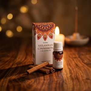 Könnte beinhalten: Eine kleine bernsteinfarbene Glasflasche mit Goloka Srilankan Cinnamon reinem Aromaöl mit weißem Verschluss, begleitet von der passenden rechteckigen Pappschachtel mit dekorativem Mandalamuster und drei braunen Zimtstangen davor.