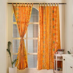 Peut inclure: Deux rideaux à motifs orange et jaune avec un design géométrique. Les rideaux sont suspendus à une tringle à rideaux noire.