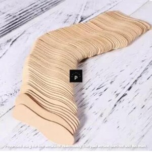 May include: A stack of light brown wooden tongue depressors, arranged in a curved shape. The depressors have a smooth, flat surface and rounded ends. The image is taken from an overhead perspective, showing the texture of the wood.