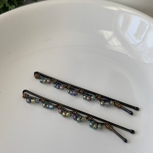 May include: Two black hair clips with iridescent beads. The beads are arranged in a cascading pattern on each clip.