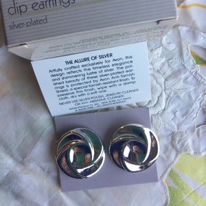 Könnte beinhalten: Silberne Clip-Ohrringe mit einem wirbelnden Design. Die Ohrringe sind in einer weißen Schachtel mit dem Text "opulent swirl clip earrings silver-plated" und "THE ALLURE OF SILVER" auf der Schachtel verpackt. Der Text auf der Schachtel enthält auch Pflegehinweise für die Ohrringe.