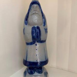 Puede incluir: Figura de cerámica de un hombre barbudo con abrigo largo y sombrero, con las manos juntas. La figura es principalmente gris con detalles azules en el sombrero, abrigo y base. La base dice "30th Edition".