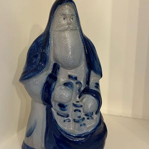 Puede incluir: Figura de cerámica de Papá Noel en tonos azules y grises. La figura tiene una larga barba y sostiene un saco. La figura está esmaltada y tiene un acabado brillante. La figura de Papá Noel es un artículo decorativo.