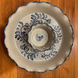 Puede incluir: Una fuente de cerámica con borde festoneado y un cuenco central para salsas. La fuente es beige con diseños florales azules y un borde azul oscuro. El cuenco para salsas también tiene un diseño floral azul.