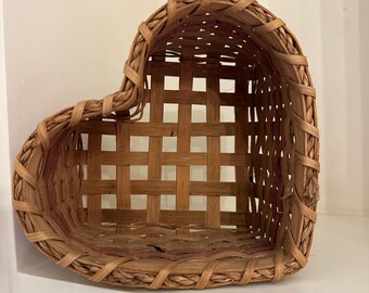 Cesta rústica de mimbre con forma de corazón y detalles en rojo.