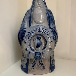 Puede incluir: Figura de cerámica de Papá Noel en tonos azules y blancos. La figura sostiene una corona con el texto "20th Issue" y los años "1984" y "2004". La figura tiene una larga barba y una túnica con capucha.
