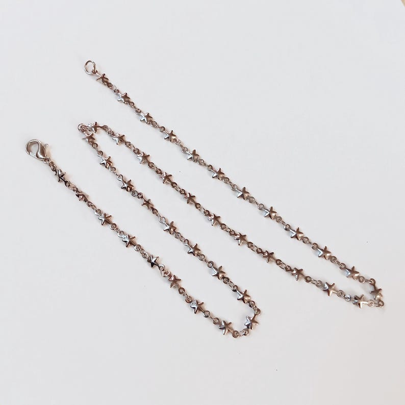 May include: Two silver star-shaped chain necklaces, one longer than the other, on a white background.