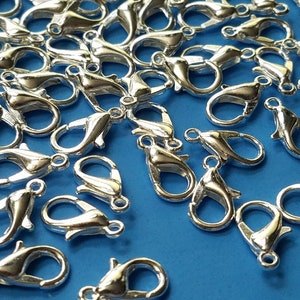 May include: A large quantity of silver-toned metal lobster claw clasps. The clasps are scattered on a blue surface.