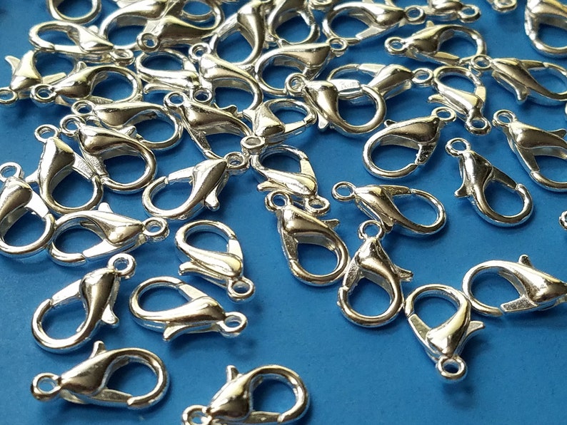 May include: A large quantity of silver-toned metal lobster claw clasps. The clasps are scattered on a blue surface.
