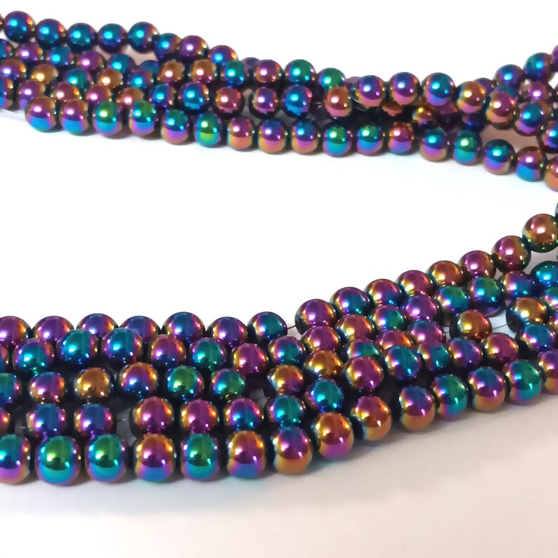 Op de afbeelding: Een streng iriserende regenboogkleurige hematiet kralen. De kralen zijn rond en glad, met een metallic afwerking. De kralen zijn geregen op een draad en klaar om te gebruiken voor het maken van sieraden.