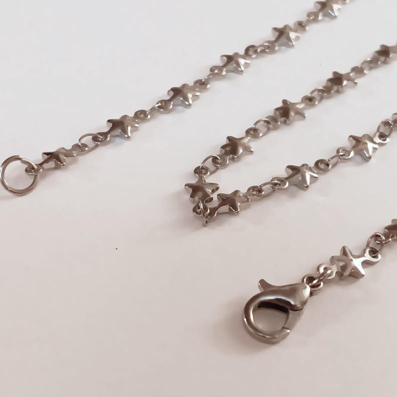 May include: A silver chain necklace with a star-shaped link design. The necklace has a lobster clasp closure.