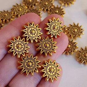 May include: Gold-toned metal star-shaped beads with a raised circular design in the center. The beads have a slightly textured surface.