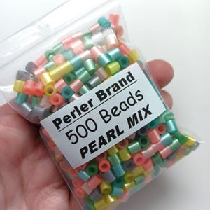 Puede incluir: Una bolsa de pl&aacute;stico transparente llena de cuentas Perler Brand. La etiqueta dice "Perler Brand 500 Beads PEARL MIX". Las cuentas cil&iacute;ndricas son de colores pastel: rosa, amarillo, verde y azul. Perfectas para manualidades.