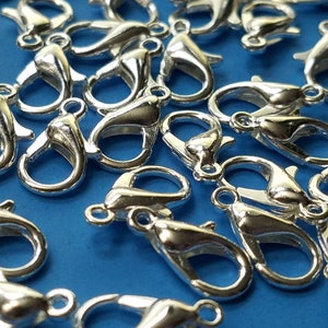 May include: A close-up of a group of silver-toned lobster claw clasps. The clasps are scattered on a blue surface.