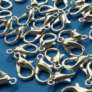 May include: A close-up of a pile of silver-toned lobster claw clasps. The clasps are a popular choice for jewelry making and crafting.