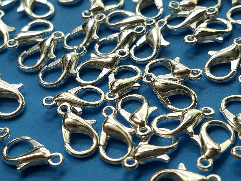 May include: A close-up of a pile of silver-toned lobster claw clasps. The clasps are a popular choice for jewelry making and crafting.
