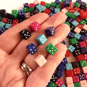 May include: A hand holding a variety of colorful dice. The dice are made of plastic and have white dots on each side. The dice are in different colors, including red, blue, green, pink, and black.