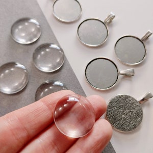 May include: Assortment of clear glass cabochons and silver-toned metal pendant trays. The cabochons are round and have a smooth, polished surface. The pendant trays are also round and have a smooth, polished surface with a silver-toned metal rim.