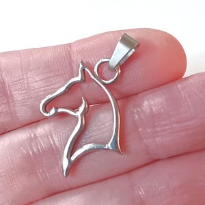 May include: Silver-toned metal pendant in the shape of a horse's head. The pendant is a cutout design, with a simple, elegant silhouette.