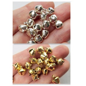 May include: A close-up of two piles of jingle bells. One pile is silver and the other is gold. The bells are small and have a hole at the top for hanging.