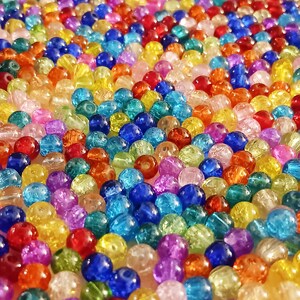 Pu&ograve; includere: Primo piano di una grande collezione di perline di vetro colorate. Le perline sono rotonde e hanno una variet&agrave; di colori, tra cui rosso, blu, verde, giallo e viola.