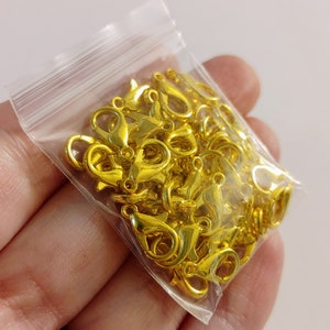 May include: A bag of gold-colored metal lobster clasps, commonly used for jewelry making.