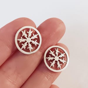 May include: A pair of silver earrings with a delicate, intricate snowflake design. The earrings are circular and have a cutout design, revealing the skin underneath.