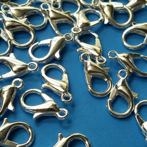 May include: A close-up of a group of silver-toned lobster claw clasps. The clasps are scattered on a blue surface.