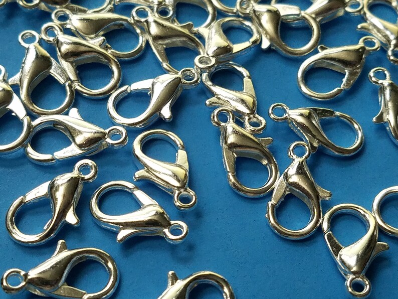 May include: A close-up of a group of silver-toned lobster claw clasps. The clasps are scattered on a blue surface.