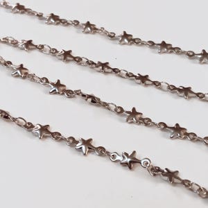 May include: Four strands of silver chain with star-shaped links. The chains are arranged in a staggered pattern on a white surface.