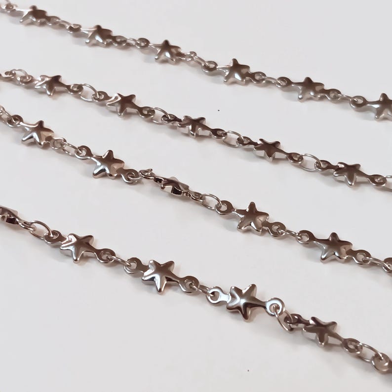 May include: Four strands of silver chain with star-shaped links. The chains are arranged in a staggered pattern on a white surface.