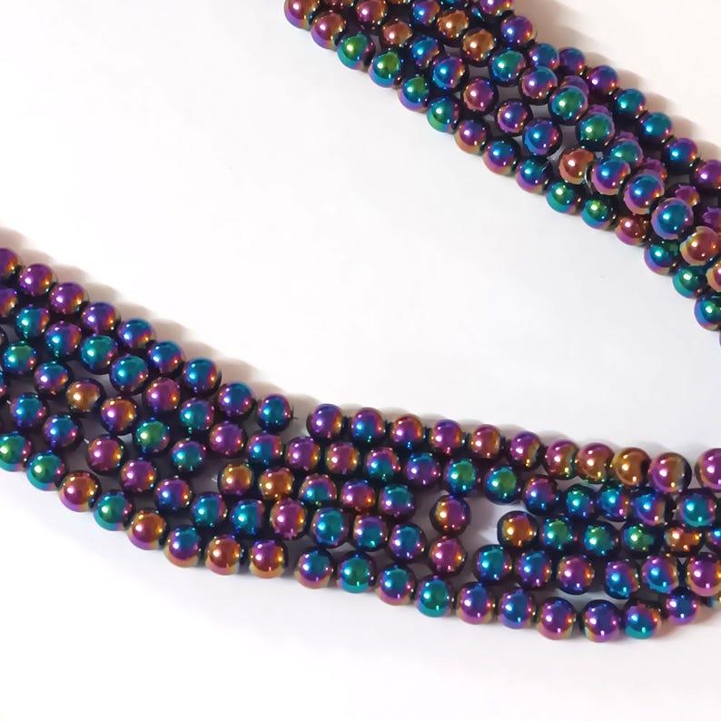 Op de afbeelding: Een streng iriserende hematiet kralen. De kralen zijn rond en hebben een metallic afwerking met tinten van paars, blauw, groen en goud.