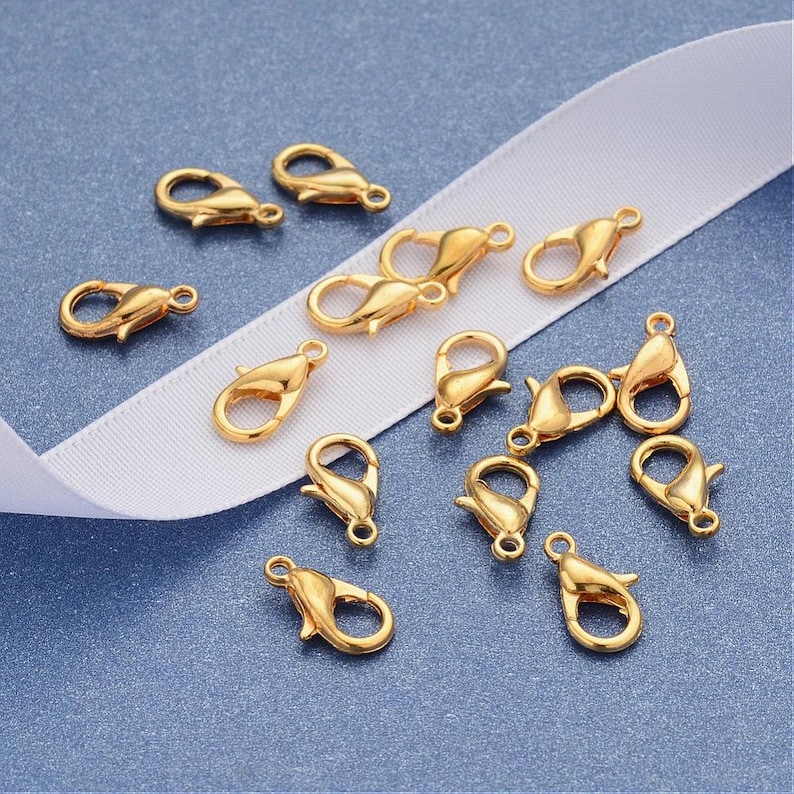 May include: A collection of 15 gold-toned metal lobster claw clasps, commonly used for jewelry making.