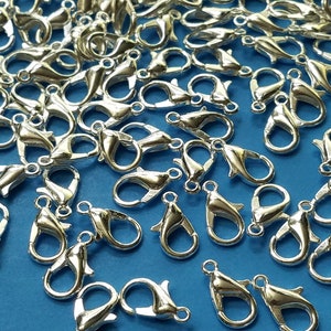May include: A close-up of a pile of silver-toned lobster claw clasps. The clasps are scattered on a blue surface.