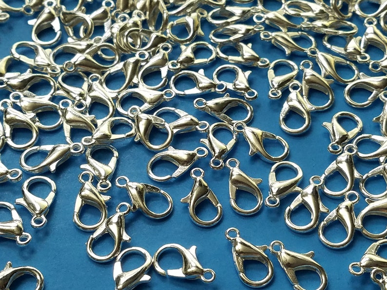 May include: A close-up of a pile of silver-toned lobster claw clasps. The clasps are scattered on a blue surface.