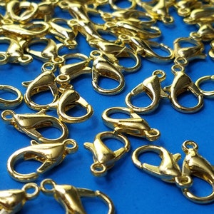 May include: A close-up of a group of gold-toned metal lobster claw clasps. The clasps are scattered on a blue surface.