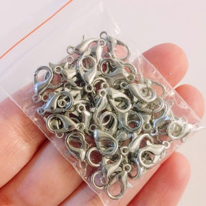 May include: A close-up of a bag of silver lobster claw clasps. The clasps are arranged in a pile and are ready to be used for jewelry making.