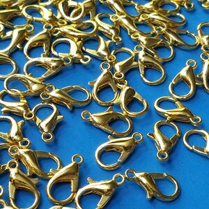 May include: A large group of gold-colored metal lobster claw clasps. The clasps are scattered on a blue surface.