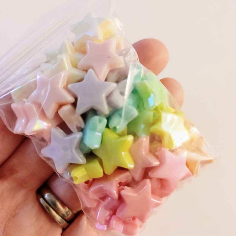 K&ouml;nnte beinhalten: Eine T&uuml;te mit pastellfarbenen sternf&ouml;rmigen Perlen. Die Perlen sind aus Kunststoff und haben eine gl&auml;nzende Oberfl&auml;che.