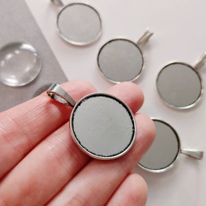 May include: A set of six silver-toned round pendant trays with a smooth, white surface. The trays have a loop at the top for hanging.