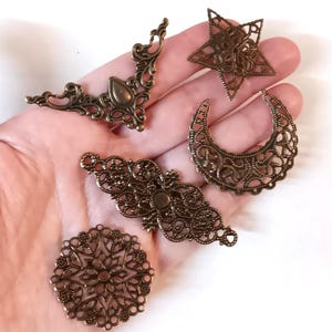 May include: Five antique gold metal filigree embellishments with intricate designs, including a crescent moon, a star, a circle, and two ornate shapes.